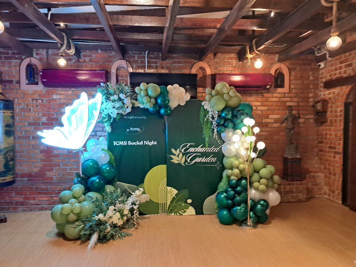 Green and white balloon arch with a neon butterfly decoration in a brick-walled room.