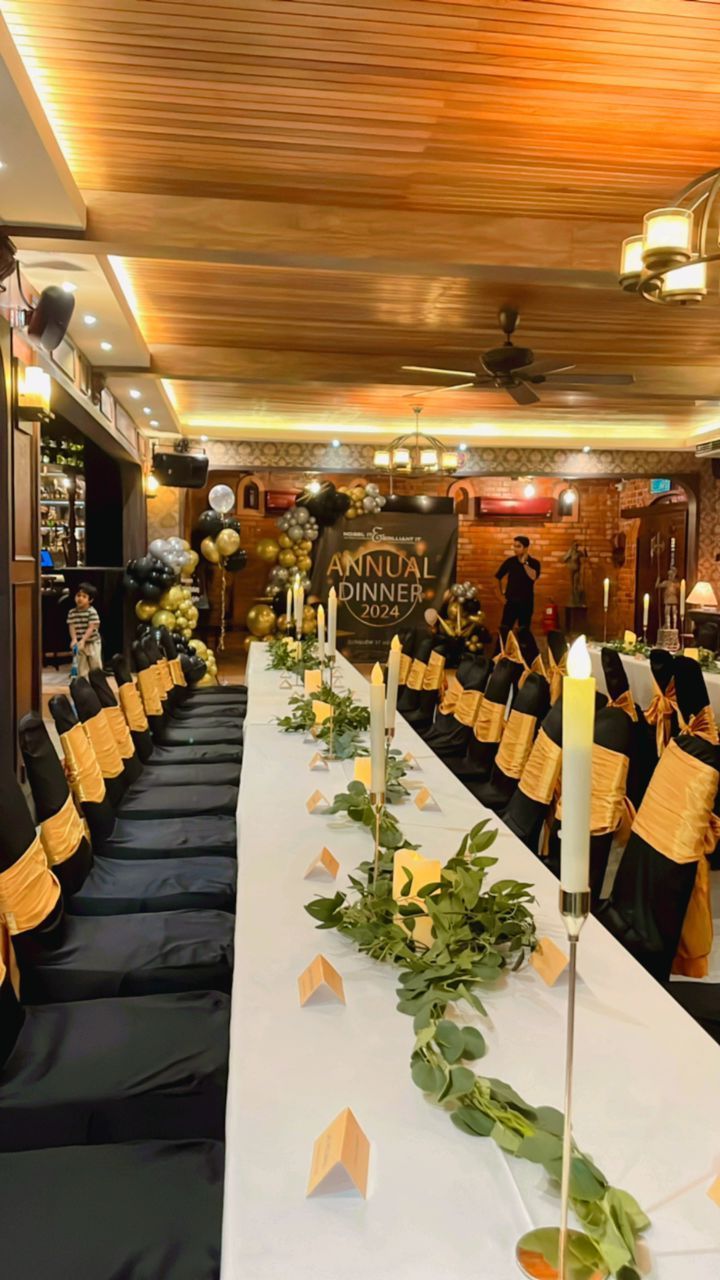 Long banquet table set for a formal event, black and gold decor, with greenery and candles.
