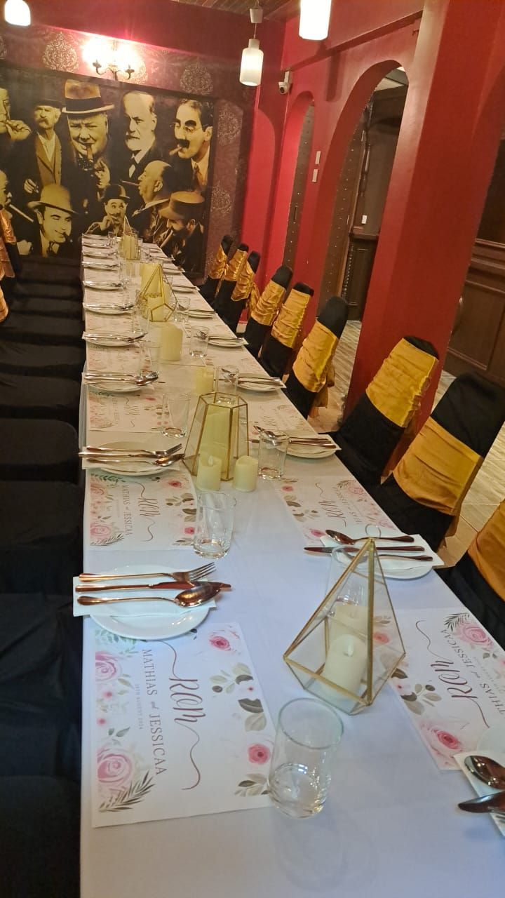 Long table set for a meal in a restaurant with floral placemats and gold accents.
