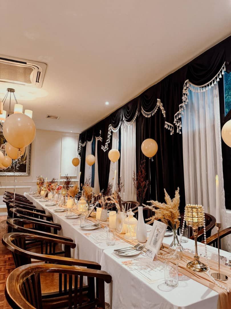 Long dining table set for an event, with gold balloons and decorations.