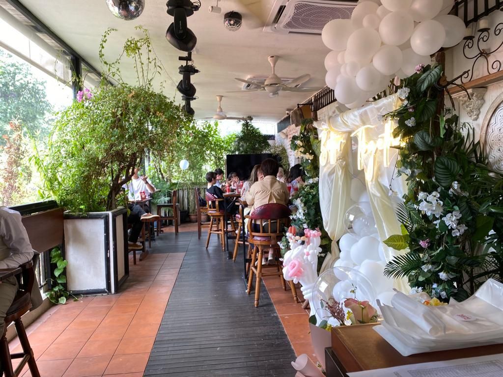Restaurant patio with plants, balloons, and seated people.