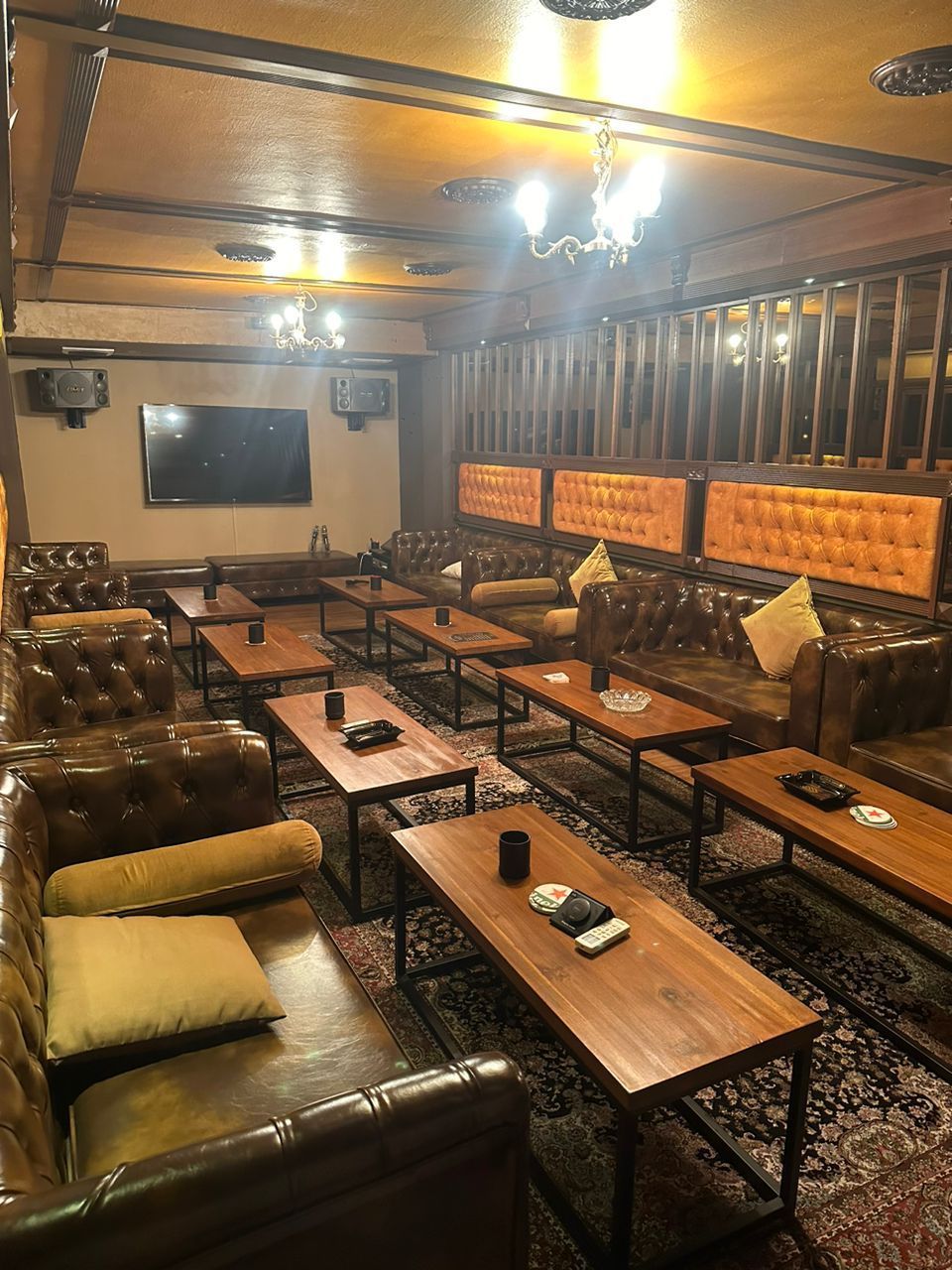 Lounge with leather sofas, wooden tables, a television, and warm lighting.