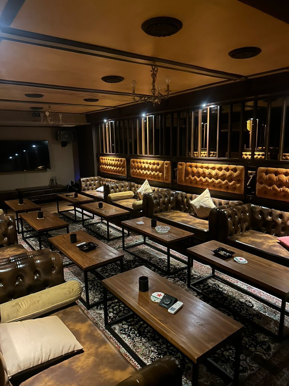 Interior of a dimly lit lounge with brown leather booths, wooden tables, and decorative ceiling.