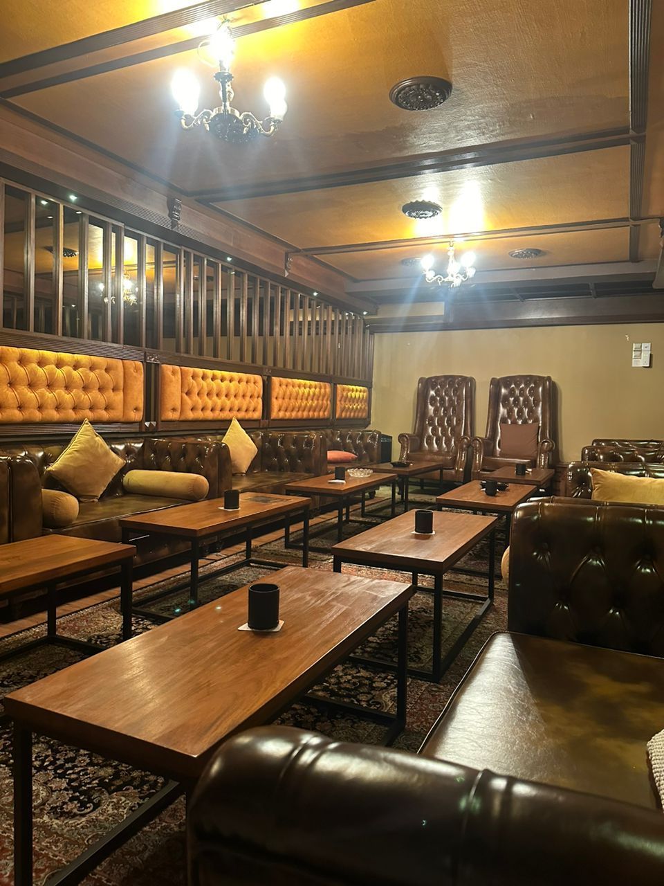 A dimly lit lounge with brown leather furniture, wooden tables, and ornate light fixtures.