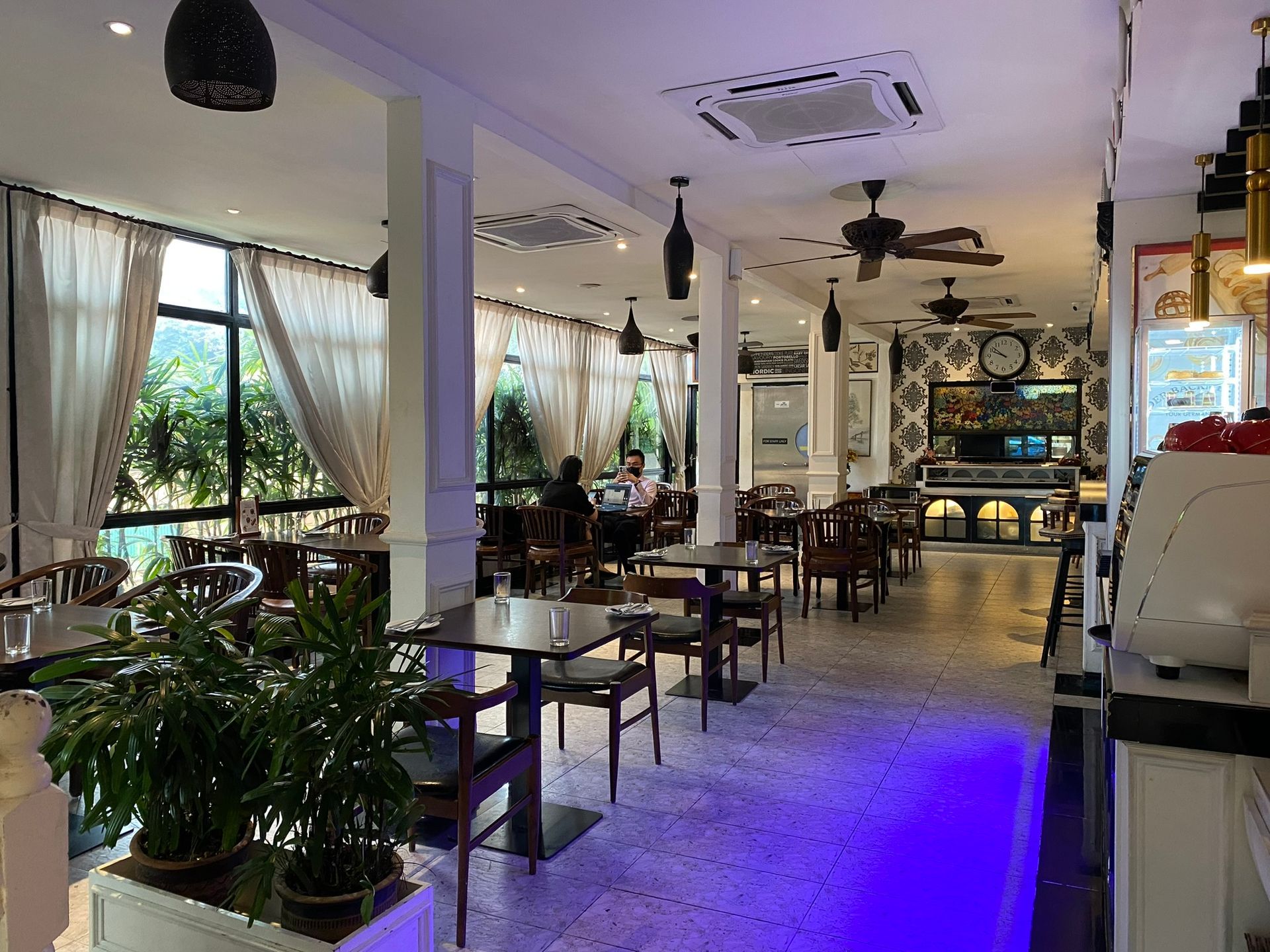 Restaurant interior with tables, chairs, and a counter, with window looking out at trees.