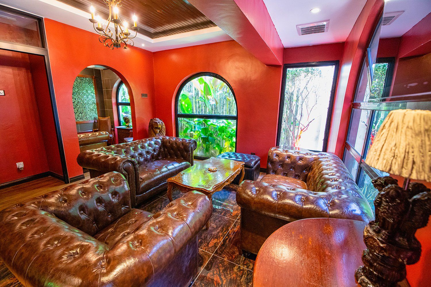 Luxurious room with leather couches, red walls, arched windows, and chandelier.