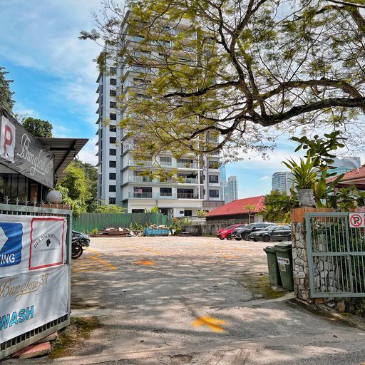 Entrance to a parking lot. Tall building in the background, trees, cars, and a sign that says