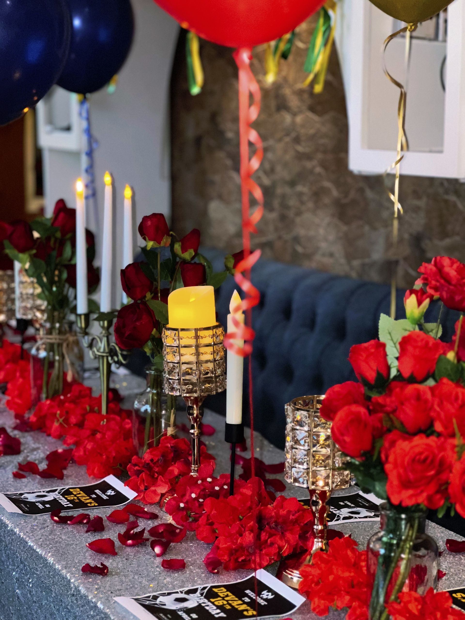 Romantic table setting with red roses, candles, and balloons; glittery tablecloth.