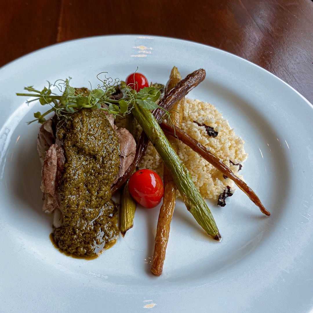 Plate of lamb with pesto sauce, roasted vegetables (carrots, asparagus), and rice.