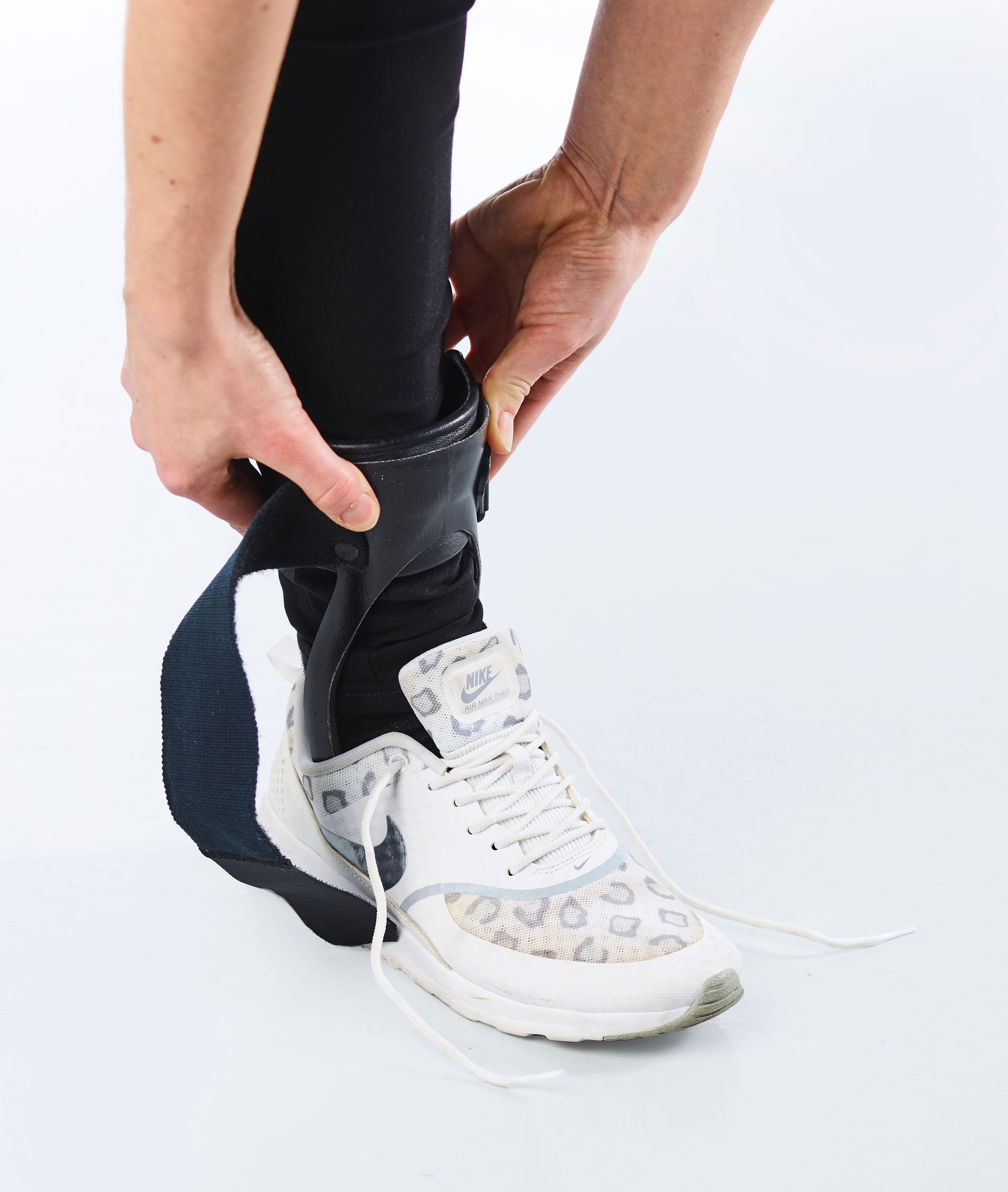 Person, der tager en sort ankelstøtte på over sorte leggings og hvide sneakers.