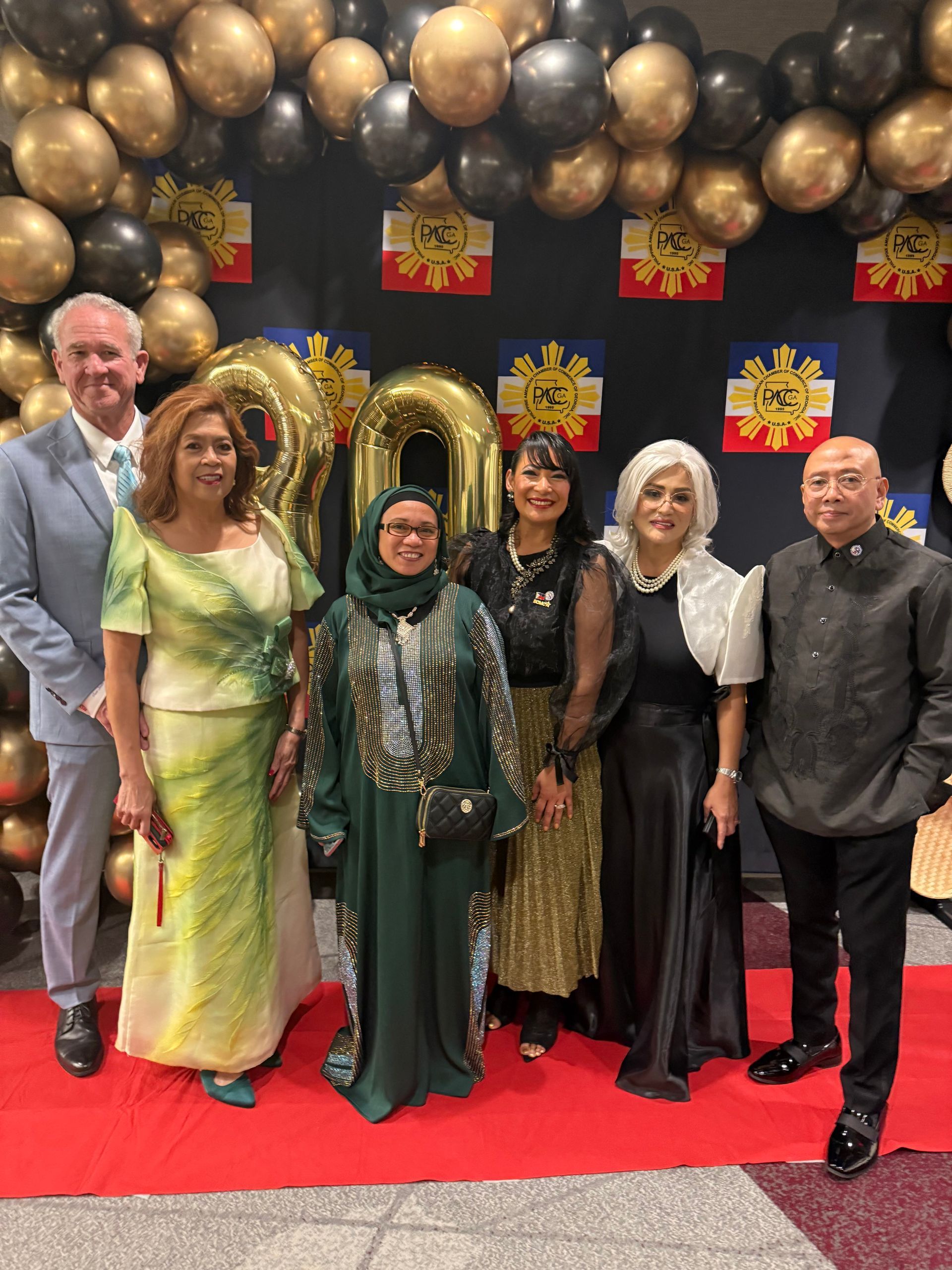 Group of people posing at an event with gold/black balloons and Philippine flags.