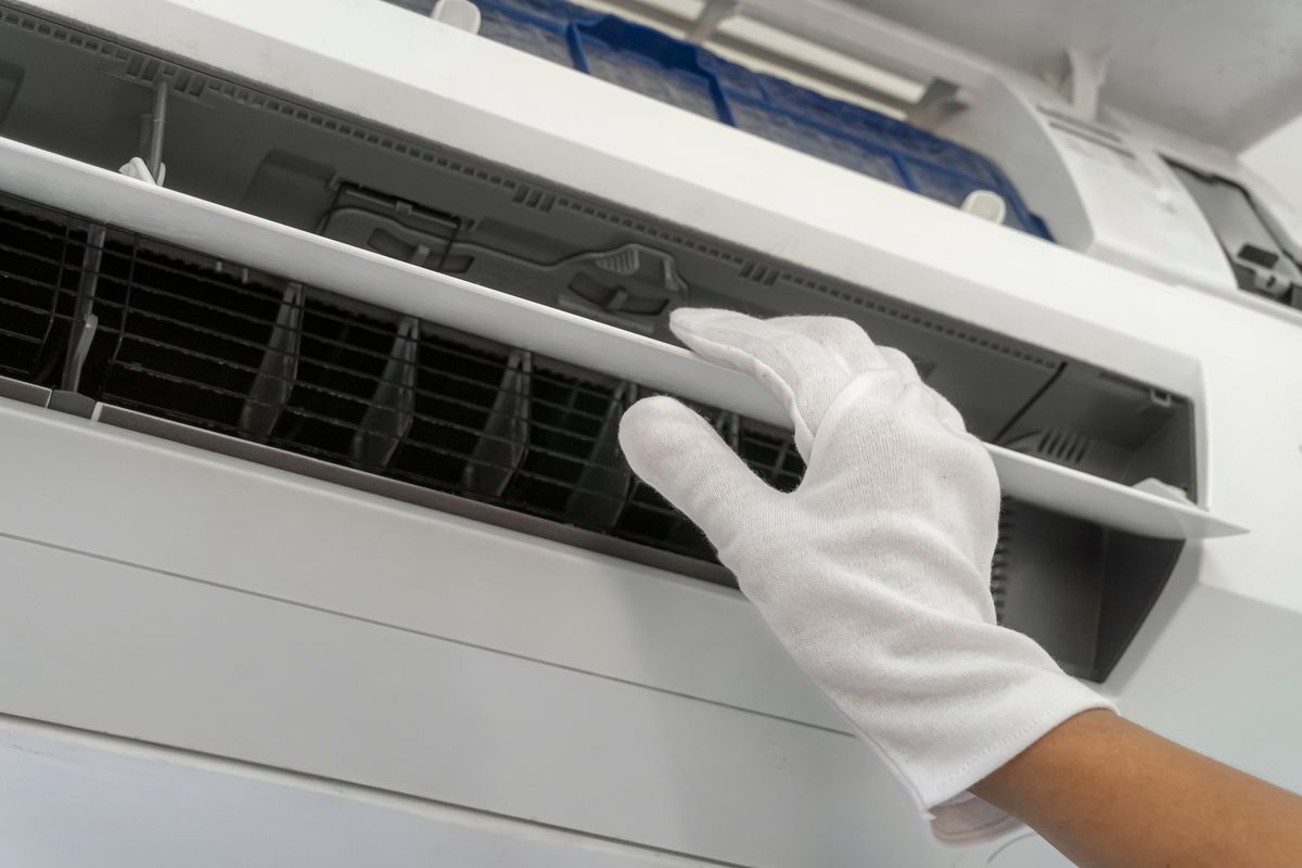 A person wearing white gloves is cleaning an air conditioner.