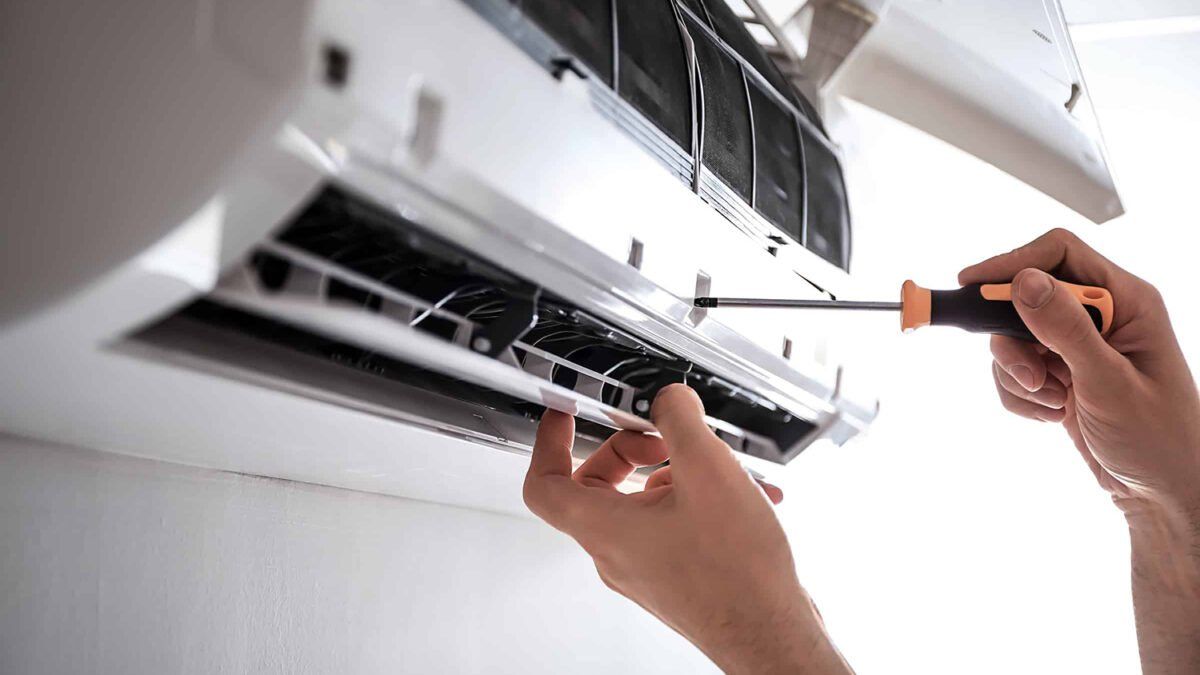 A person is fixing an air conditioner with a screwdriver.