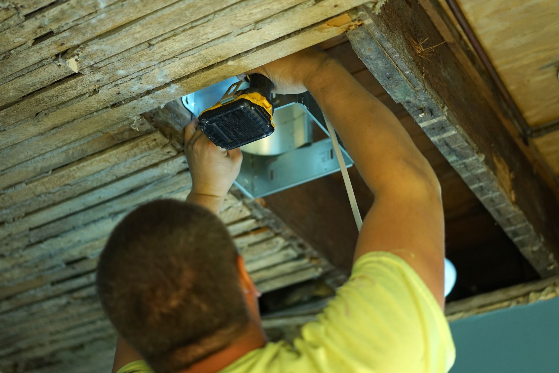 A man is working on a ceiling fan with a drill.