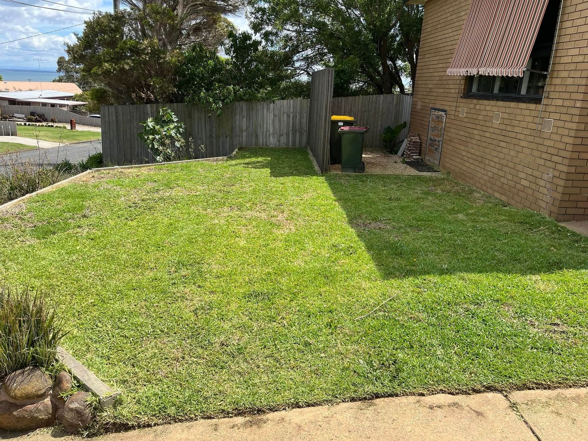 A Lush Green Backyard With a Brick House — RJT Lawn and Gardening in Drysdale, VIC