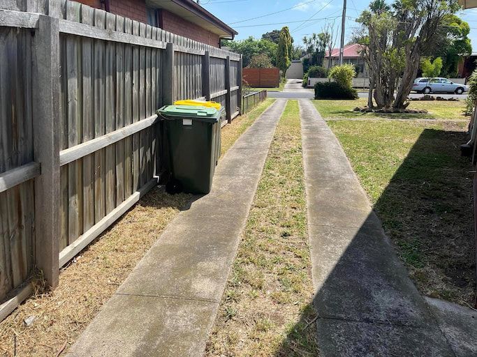 A Wooden Fence And Bins Next To Driveway — RJT Lawn and Gardening in Leopold, VIC