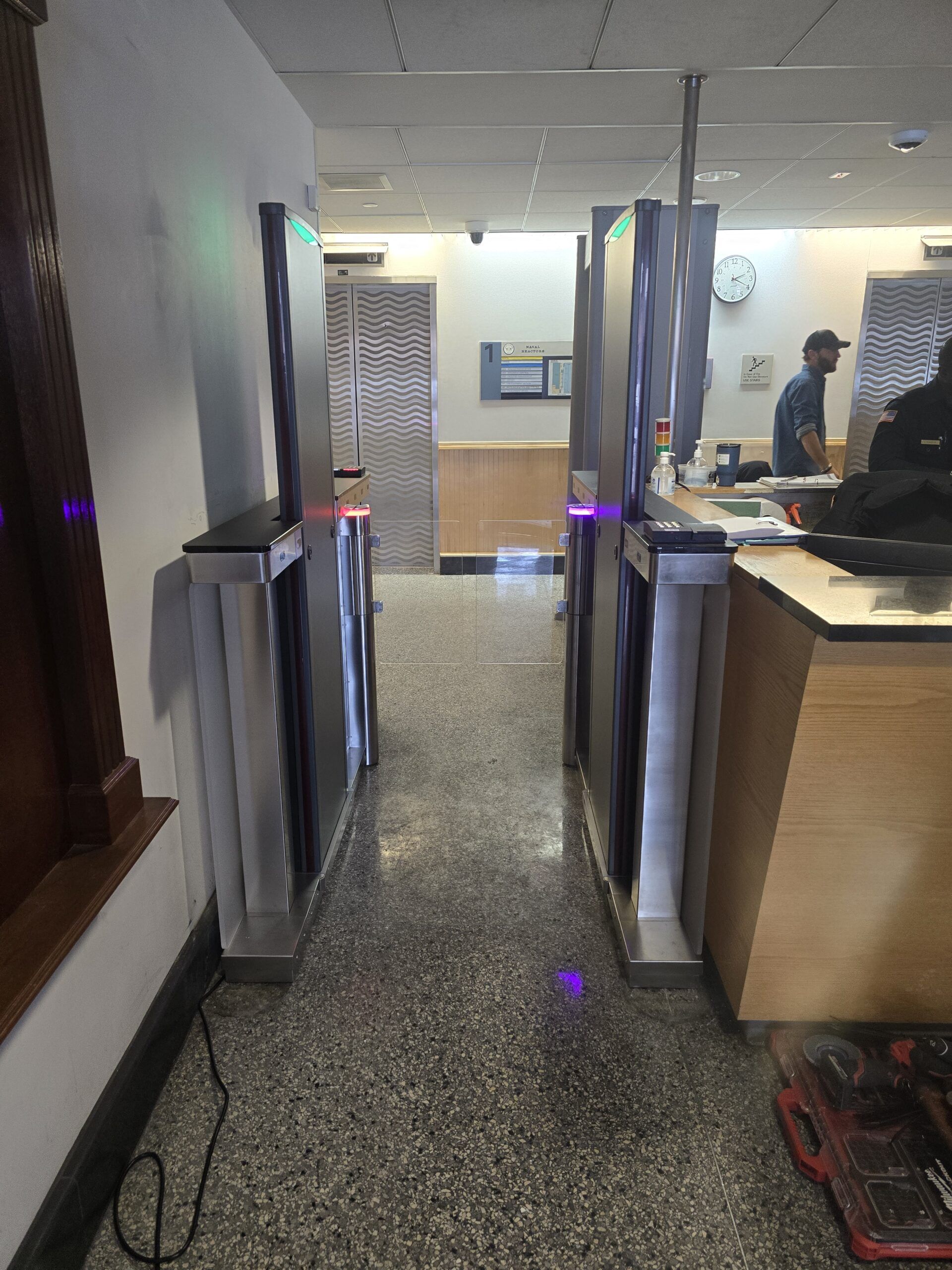 Security turnstiles in a building entrance. A man stands behind a counter.