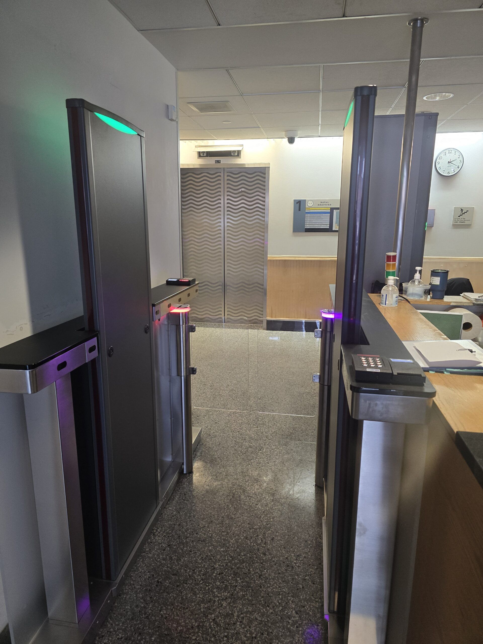 Security entrance with turnstiles and elevator in the background. Green and purple lights are visible.