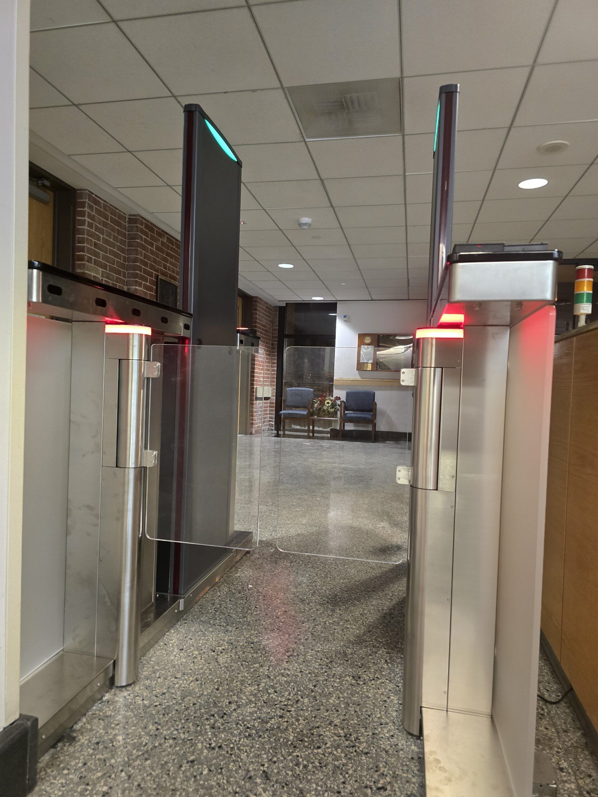 Turnstiles in an entryway with red lights on top, brick wall on the left, and a hallway beyond.