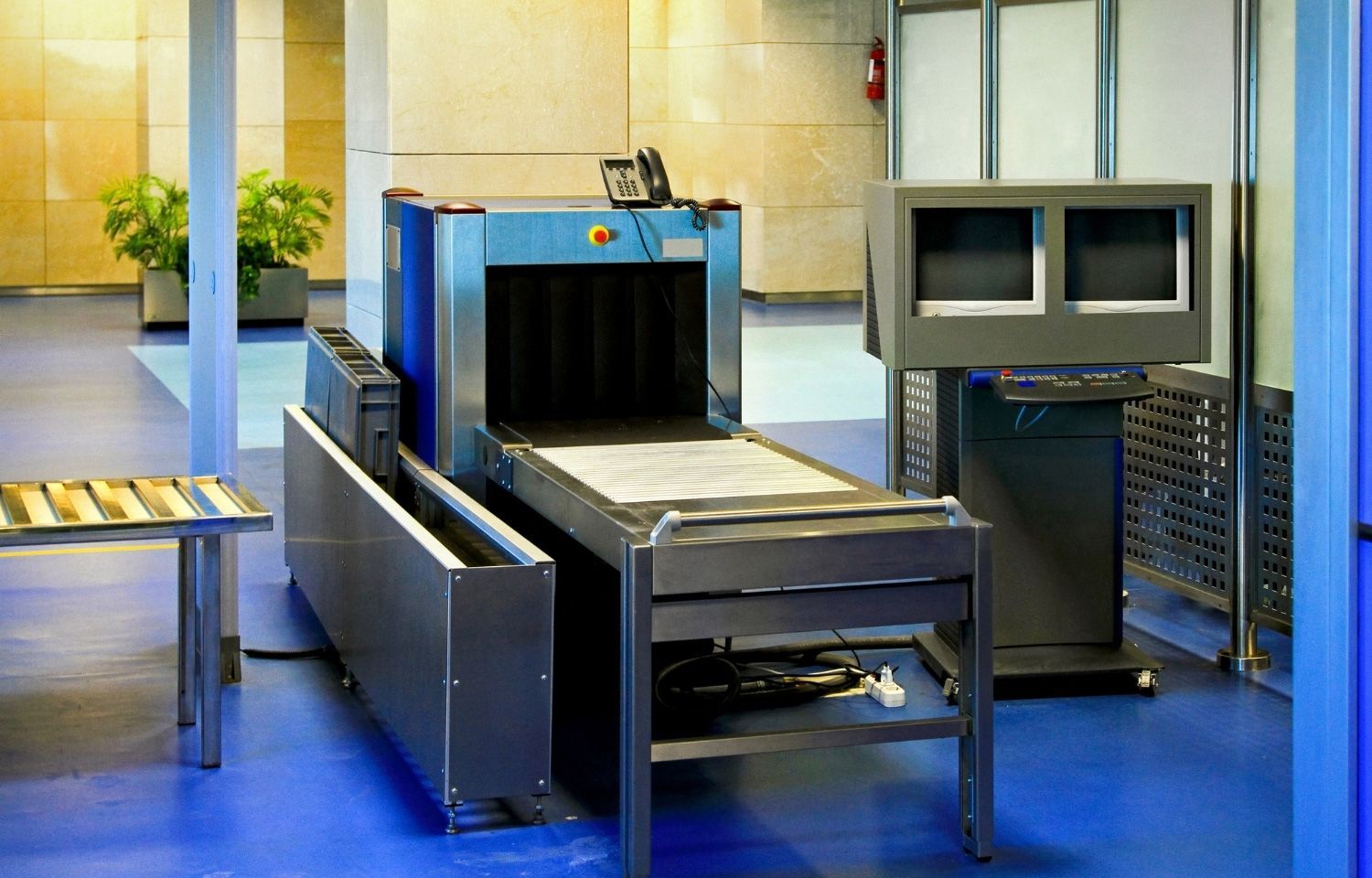 X-ray baggage scanner at airport Airport security X-ray scanner with conveyor belt, stainless steel, and monitor. Blue walls, tiled floor.