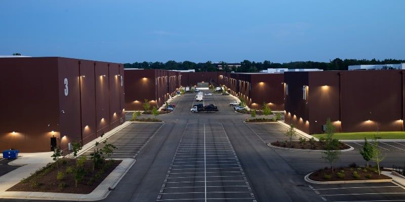 An aerial view of a brown industrial building complex at dusk with parking and landscaping.