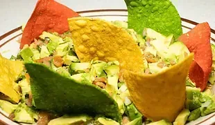 Colorful tortilla chips surround a salad of diced avocado and beans in a brown-rimmed bowl.