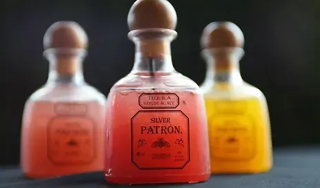 Three Patron tequila bottles, filled with colorful drinks.