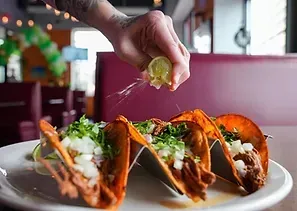Lime juice squeezed onto tacos on a white plate in a restaurant.