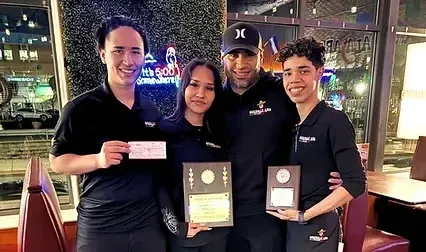 Four people, restaurant staff, holding awards and a check, smiling, indoors.