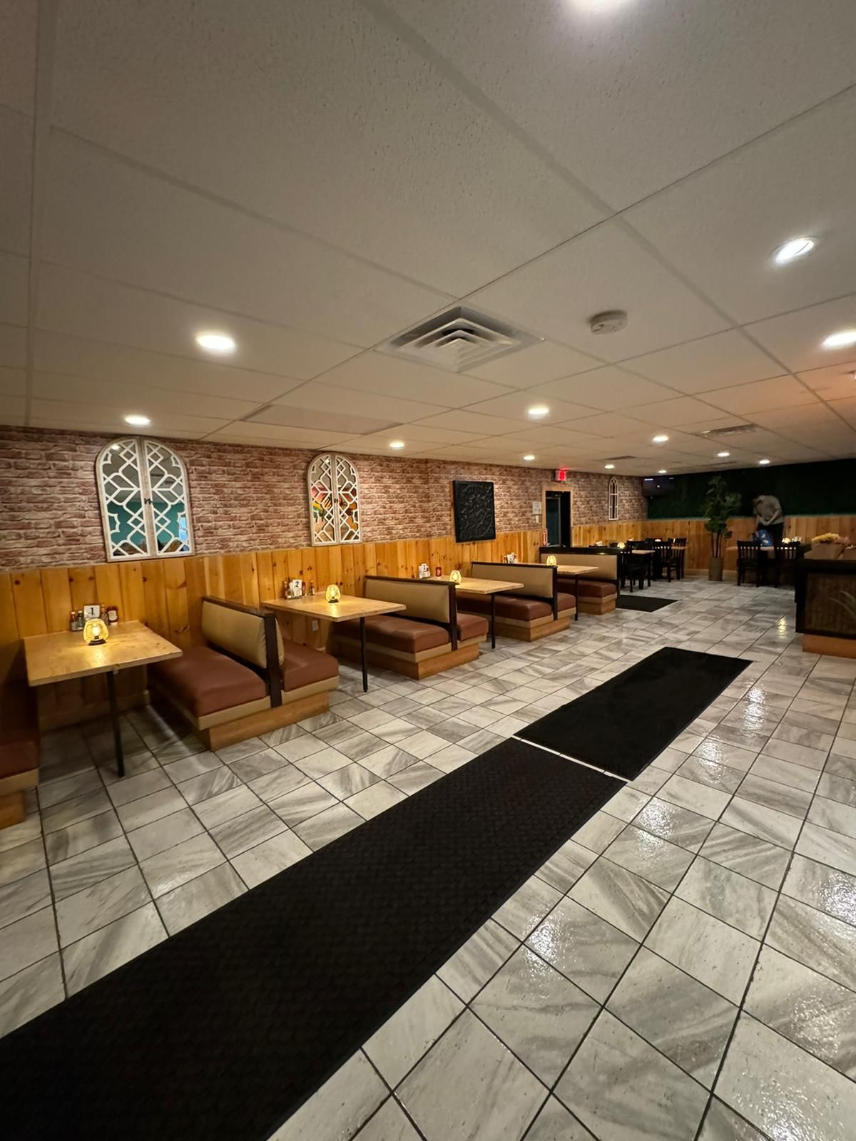 Restaurant interior with booths, tables, a brick wall, and a long black rug.