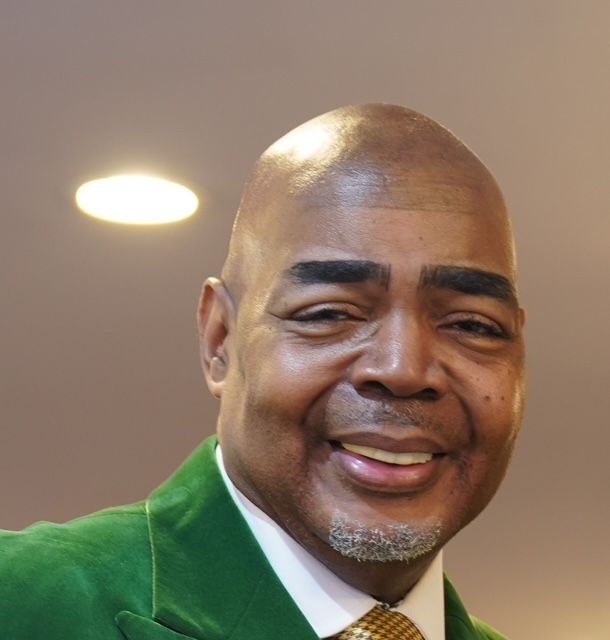 A man wearing a green jacket and tie smiles for the camera