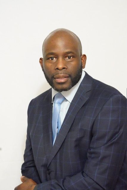 A man in a suit and tie is sitting in front of a white wall.