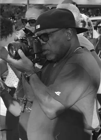 A man in a hat and sunglasses is taking a picture with a camera.