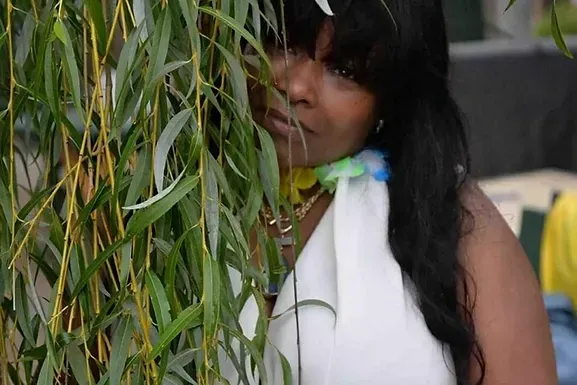 A woman in a white dress is peeking out from behind a tree.