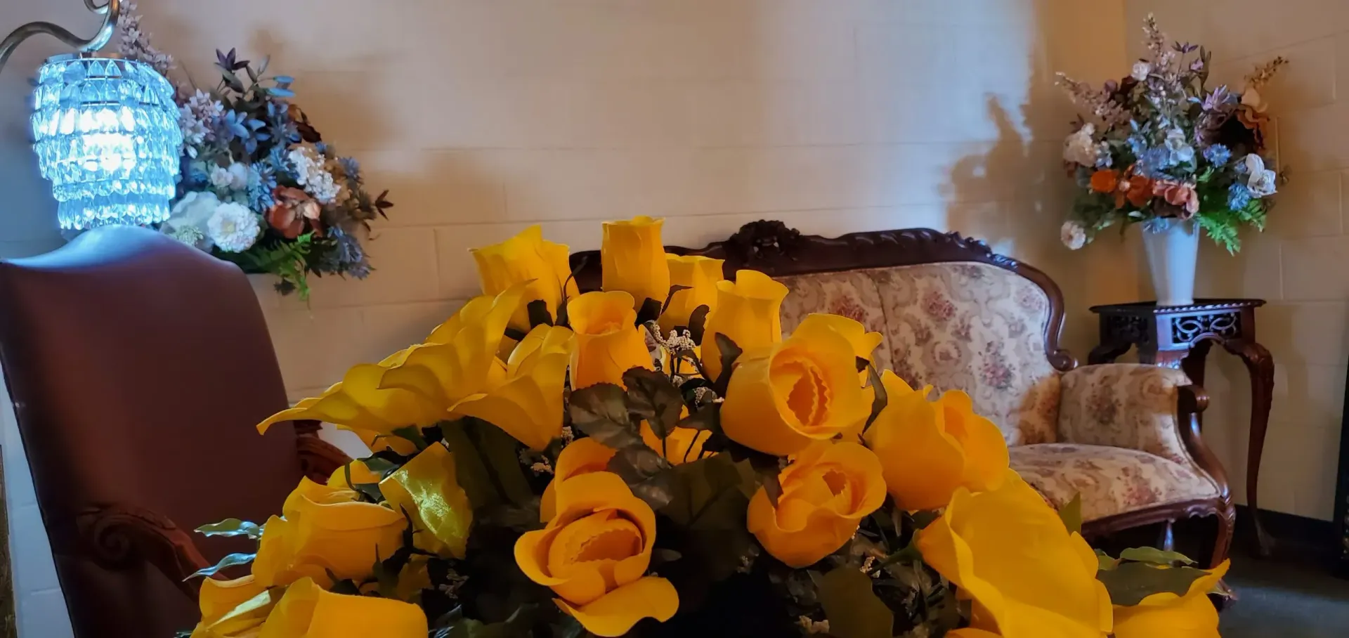 Yellow roses in a bouquet on a table with a decorative sofa, framed by floral arrangements.