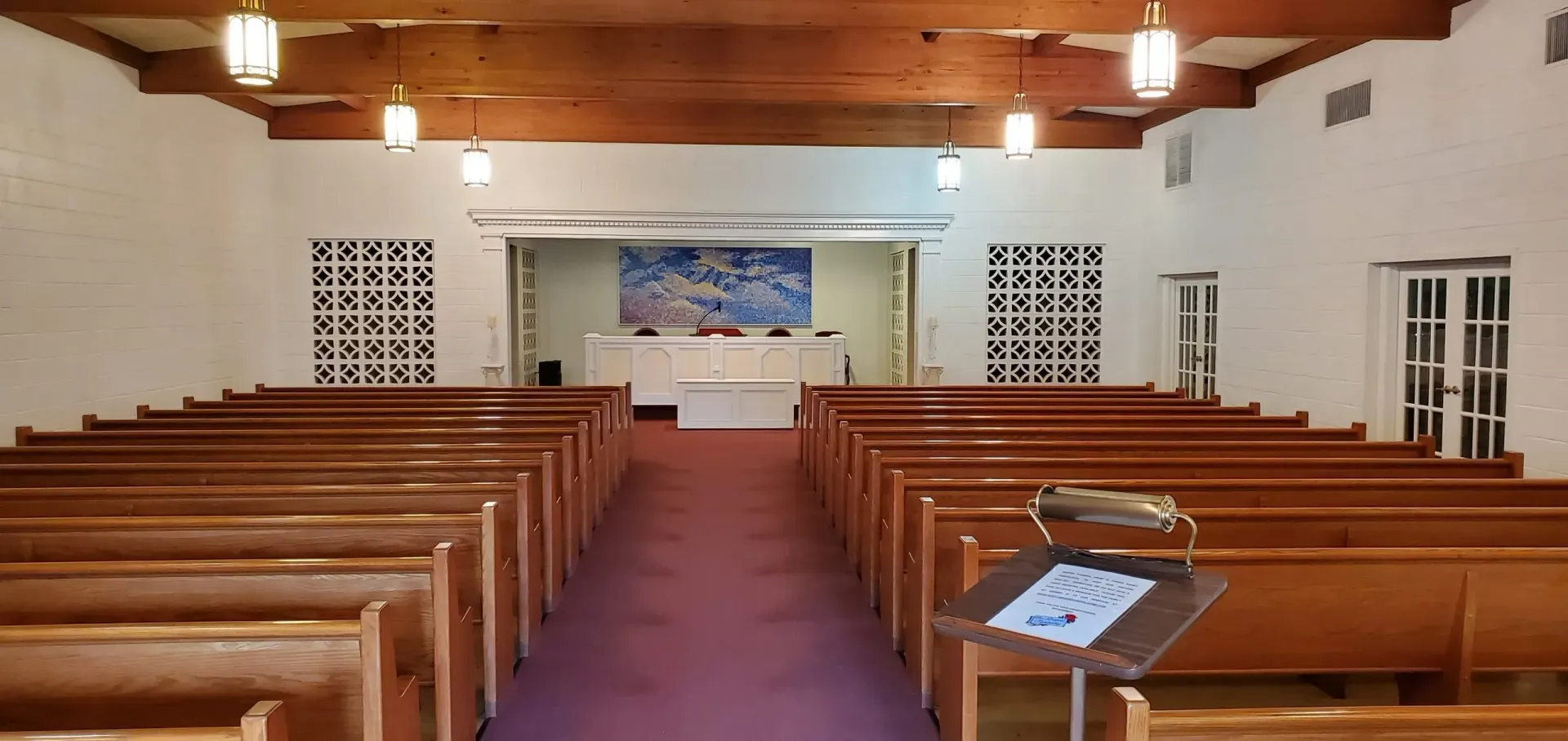 Interior view of a chapel with rows of wooden pews, a purple carpet, and a podium.