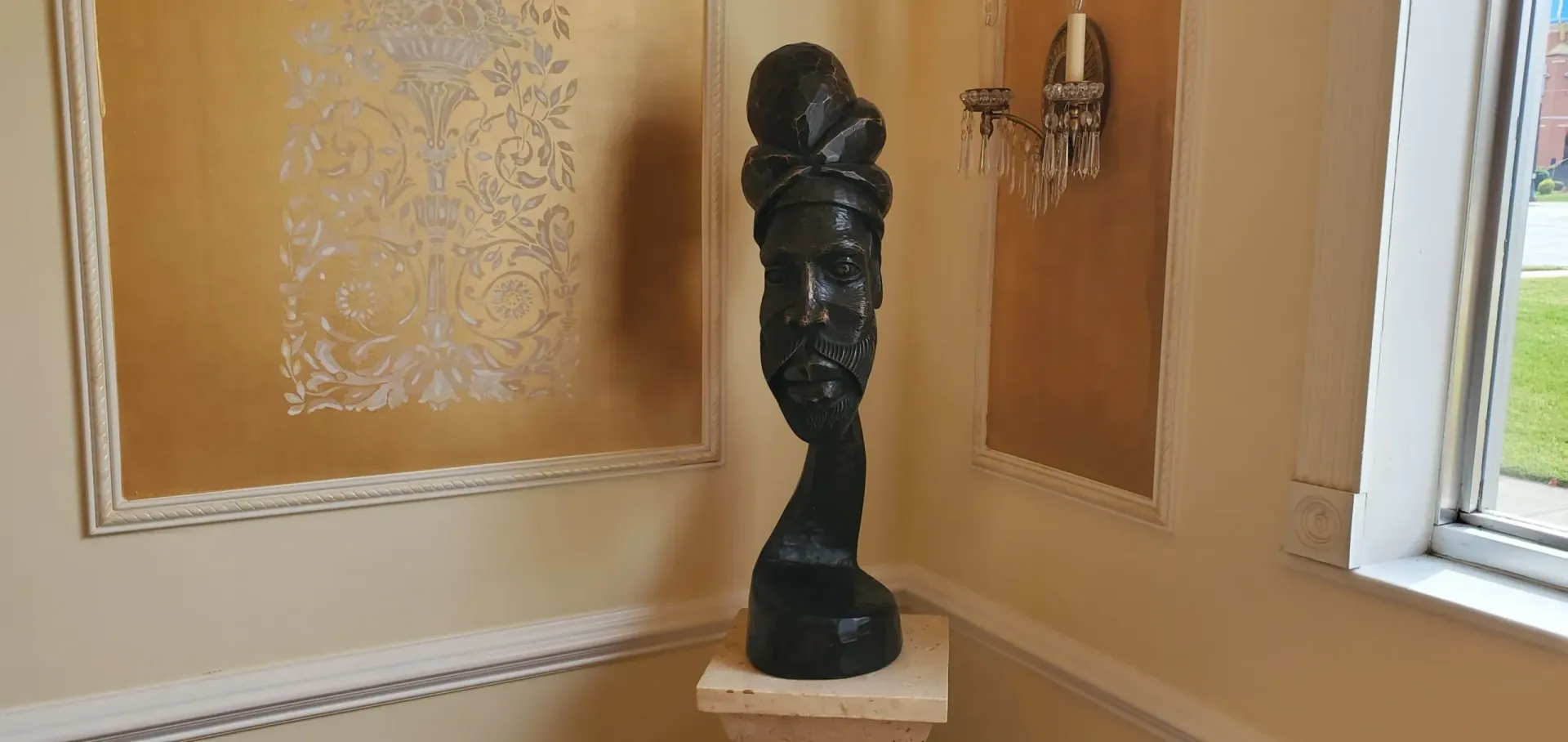 Black sculpture on a pedestal in a room with gold-colored walls and a window.