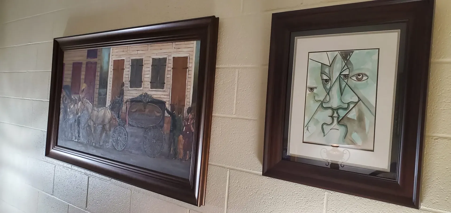 Two framed paintings hang on a light-colored brick wall.