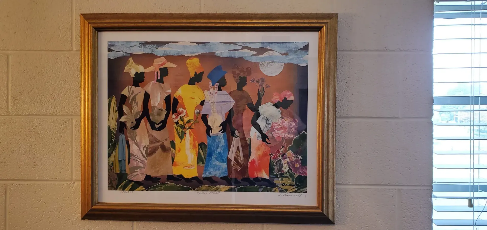 Artwork of figures in colorful clothing framed on a wall next to a window with blinds.
