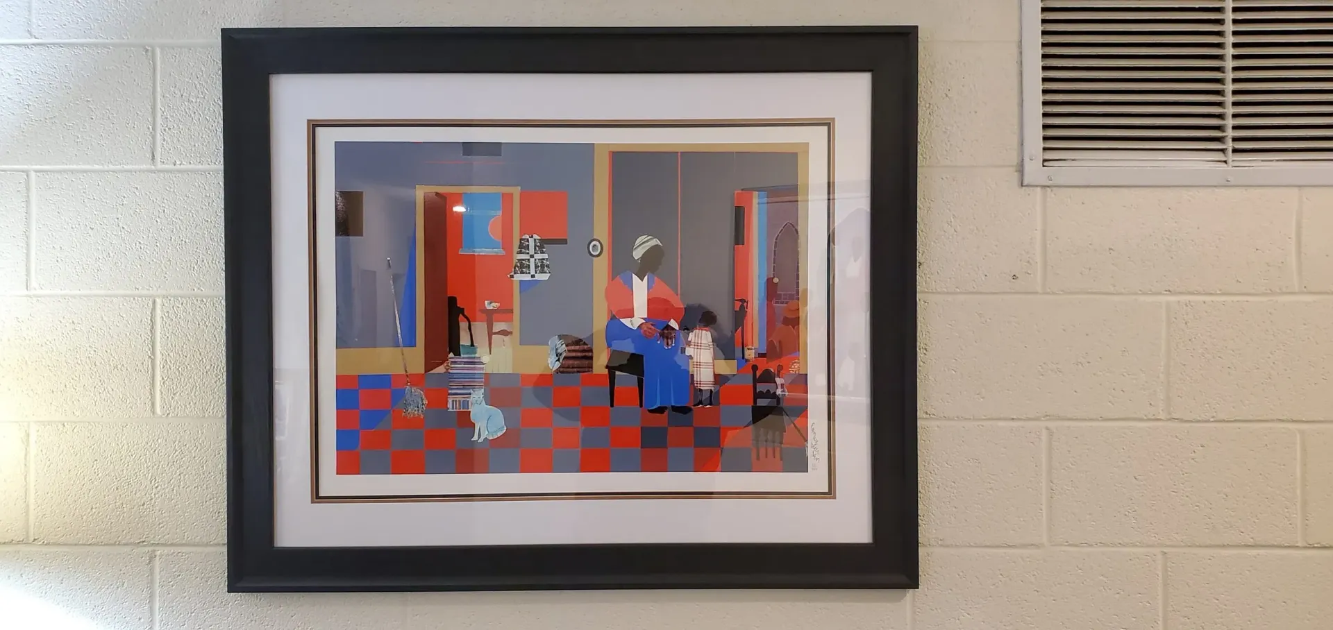 Framed artwork depicting a colorful interior scene, hanging on a beige brick wall.