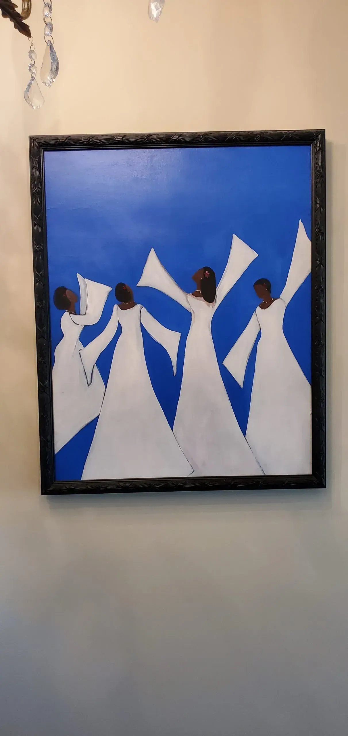 Painting of four figures in white robes with outstretched arms, against a blue background, framed in black.