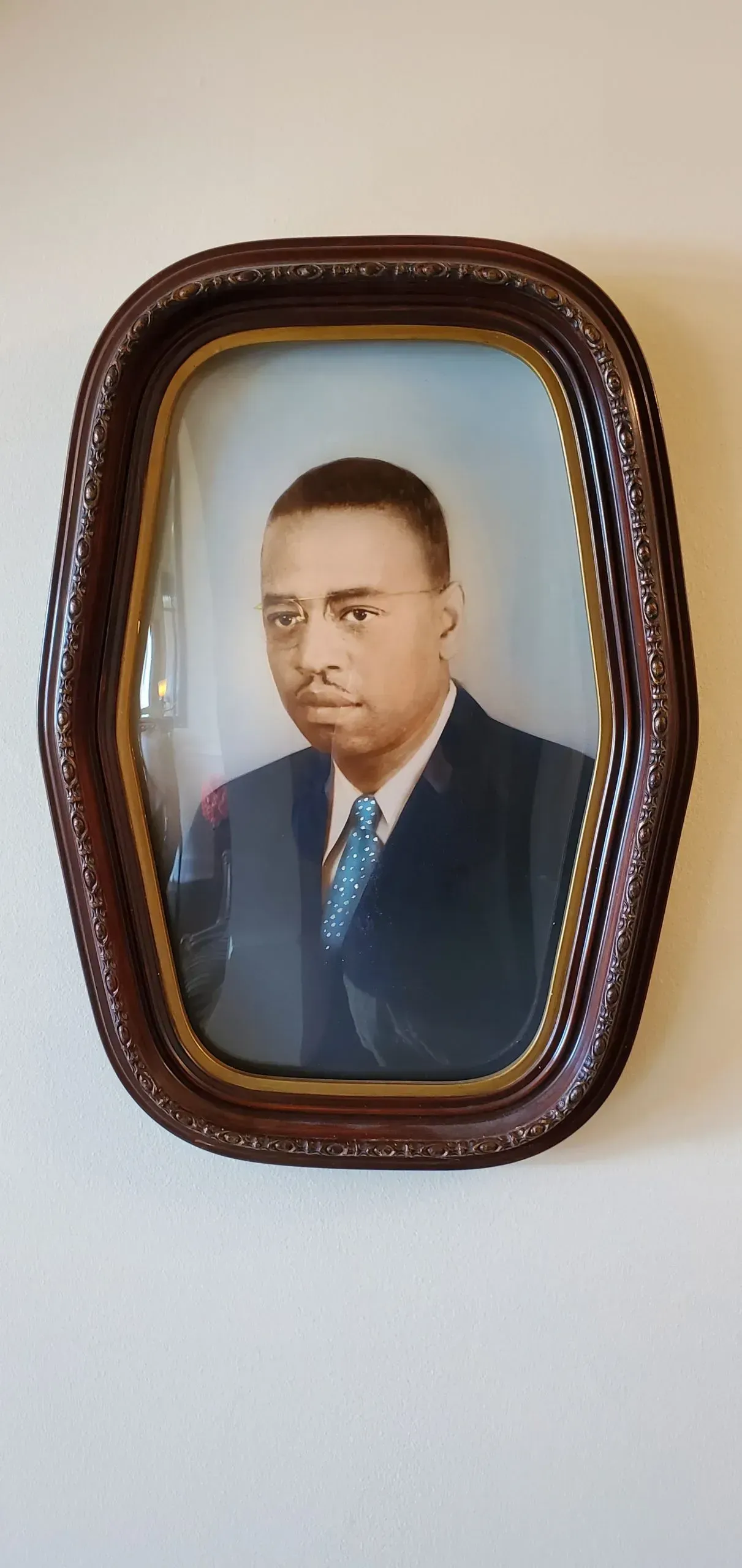 Portrait of a man in a dark suit and tie, framed in an oval, ornate wooden frame.