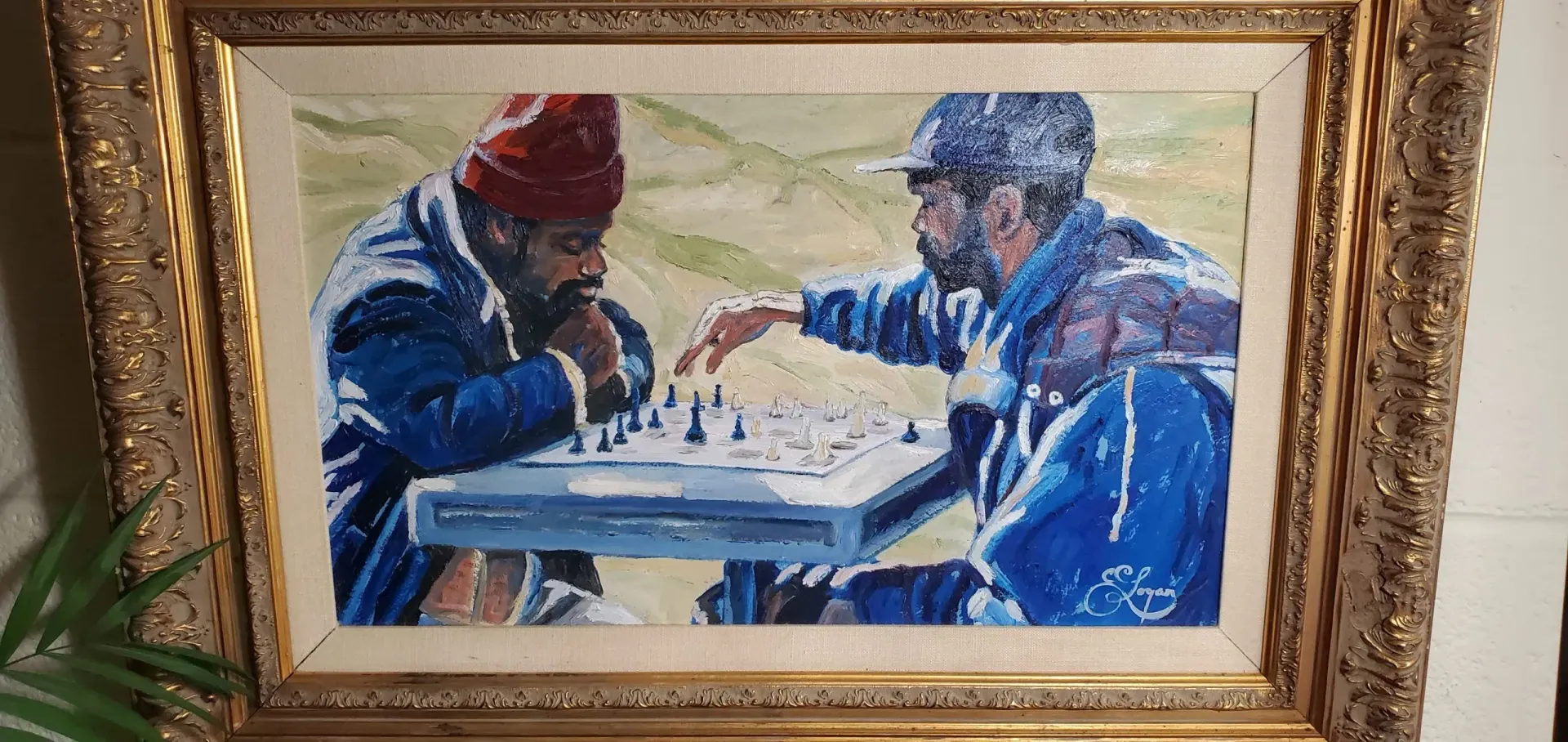 Two men playing chess in a park, painting in a gold frame. One wears a red hat, the other a cap, both in blue.