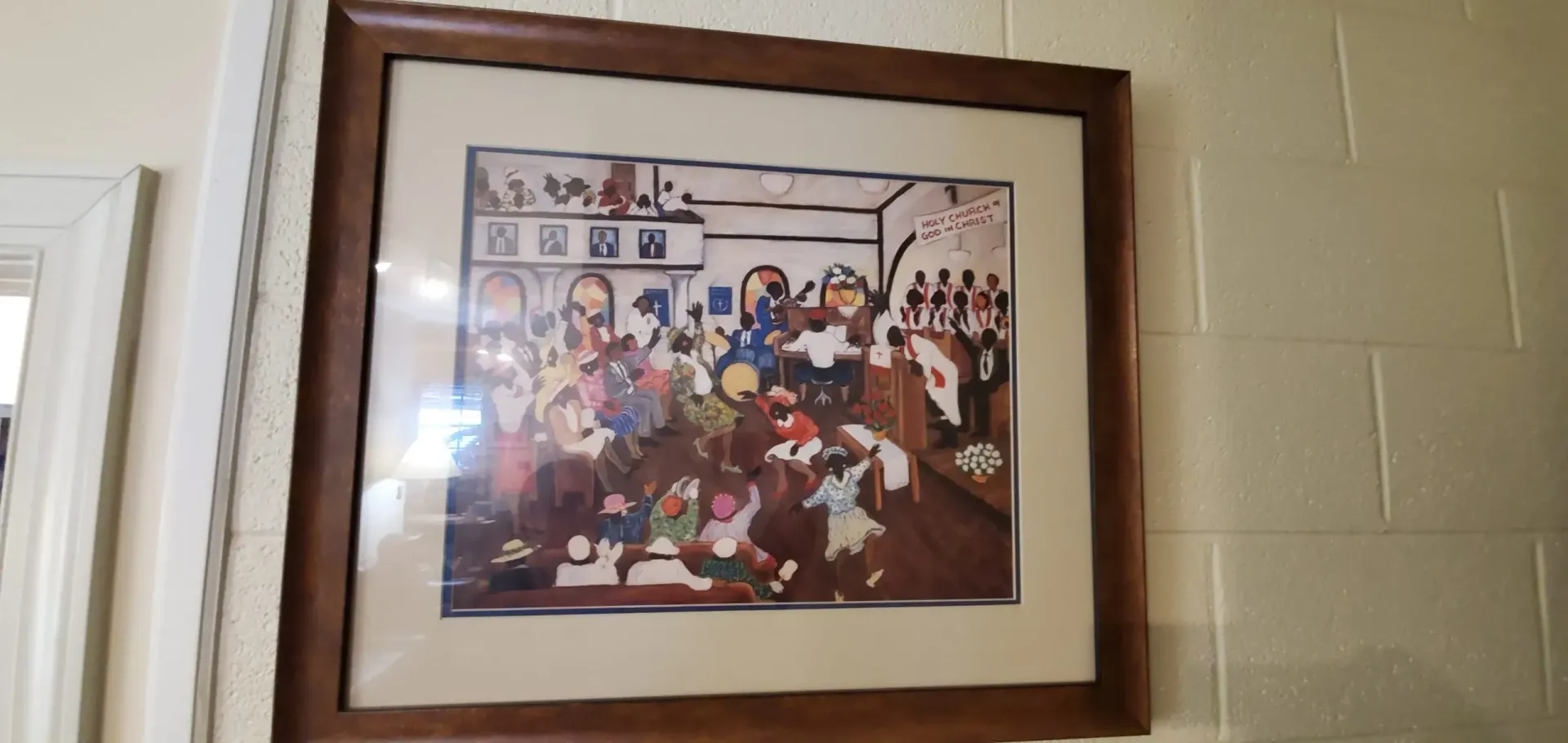 Painting of figures in a room, framed in brown, hung on a textured beige wall.