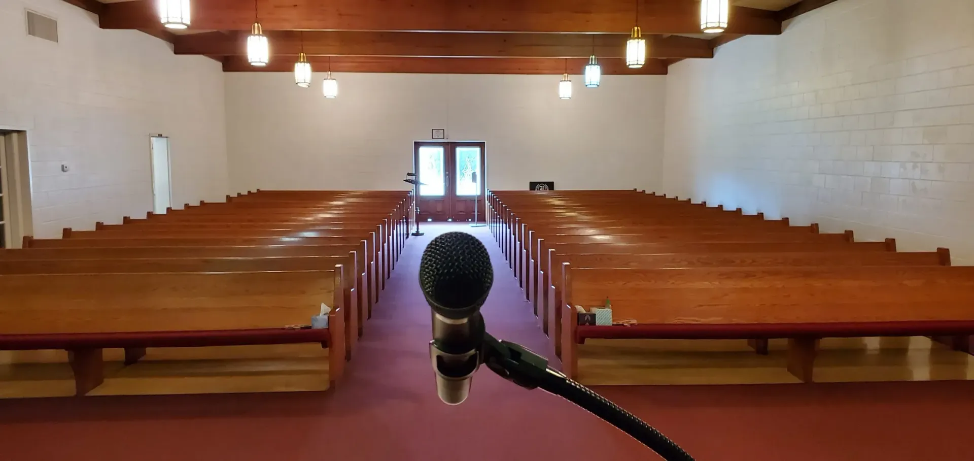 Interior of a church with wooden pews, red carpet, and a microphone in the foreground.