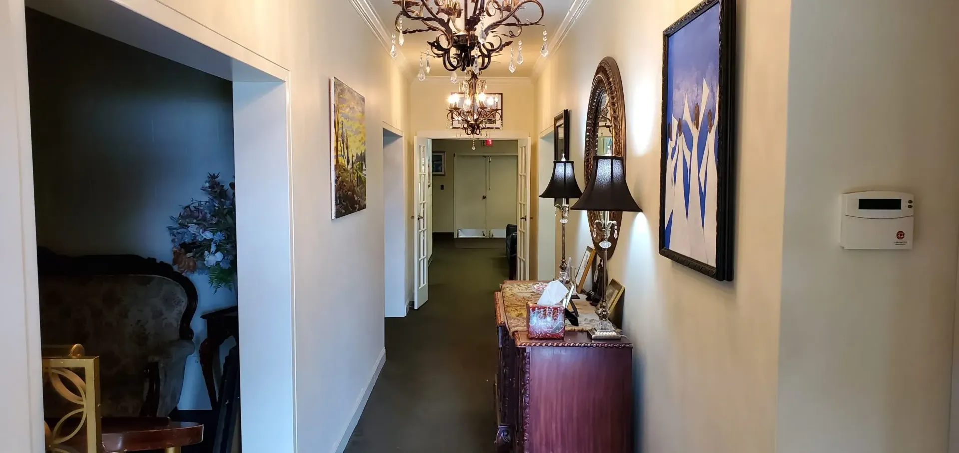 Hallway with art, lights, and a maroon dresser.