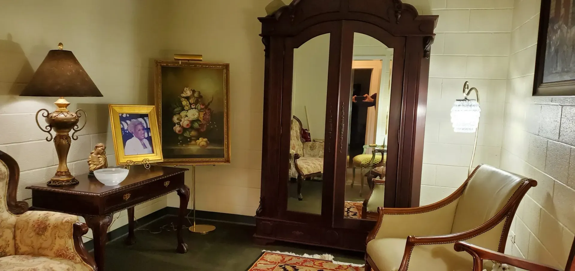 A room with antique furniture, including a wardrobe, chairs, a lamp, and artwork.