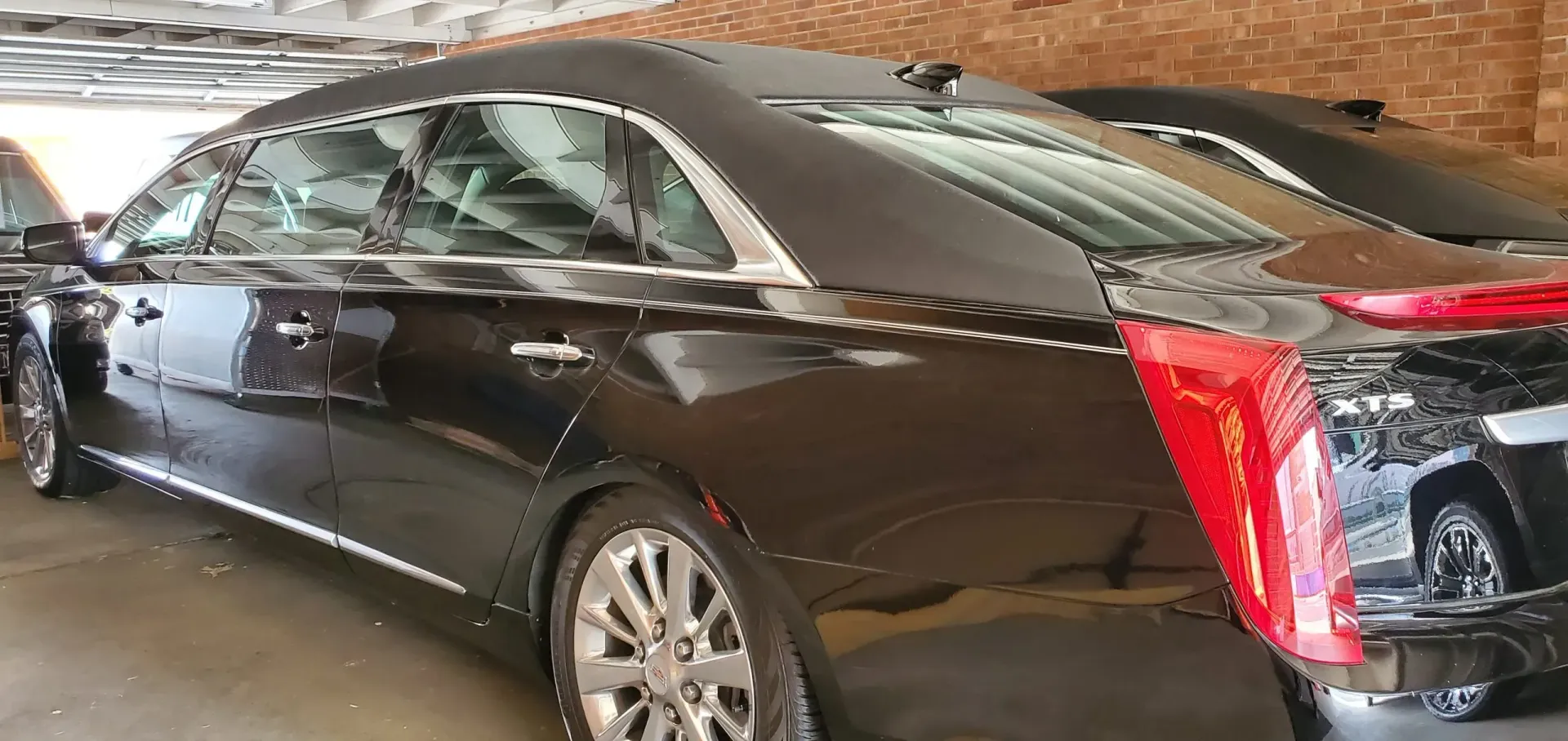 Black Cadillac sedan parked in a garage. Tail light is red. Silver trim.