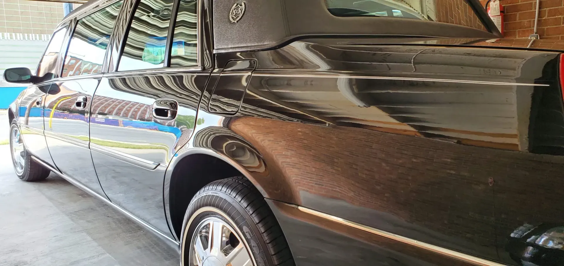 Black Cadillac limousine, close-up of the exterior. Shiny, reflecting light. The car is likely in a garage.