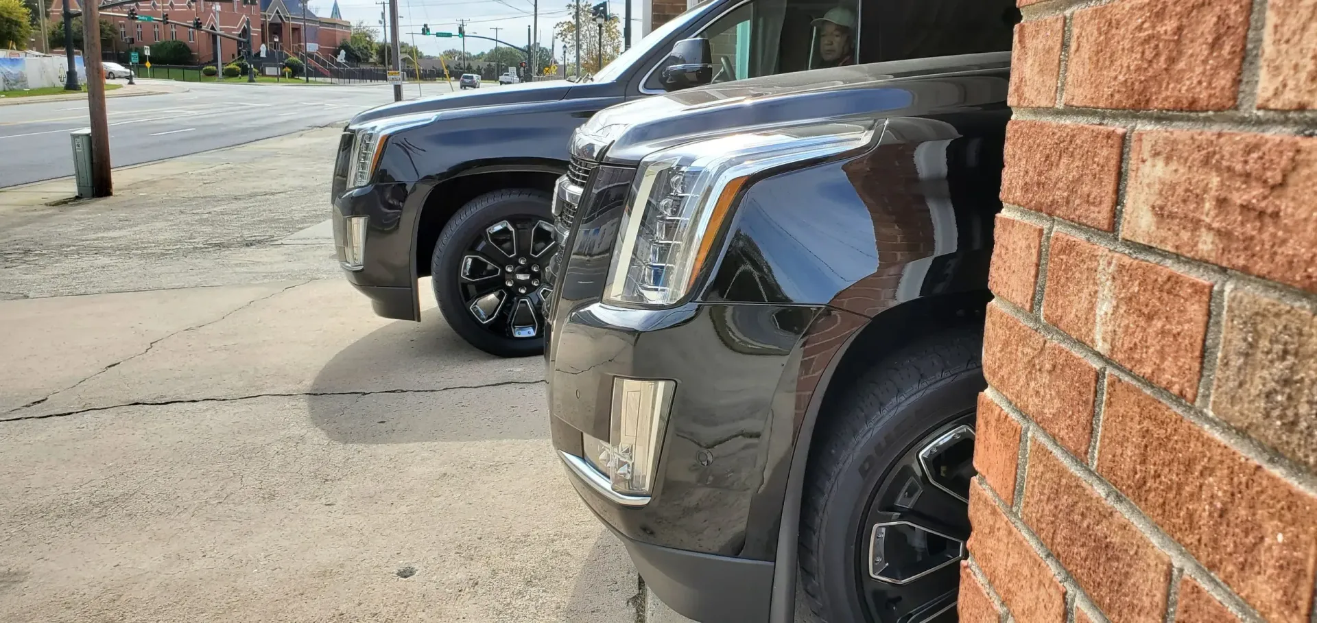 Two black SUVs parked next to a brick building on a sidewalk.